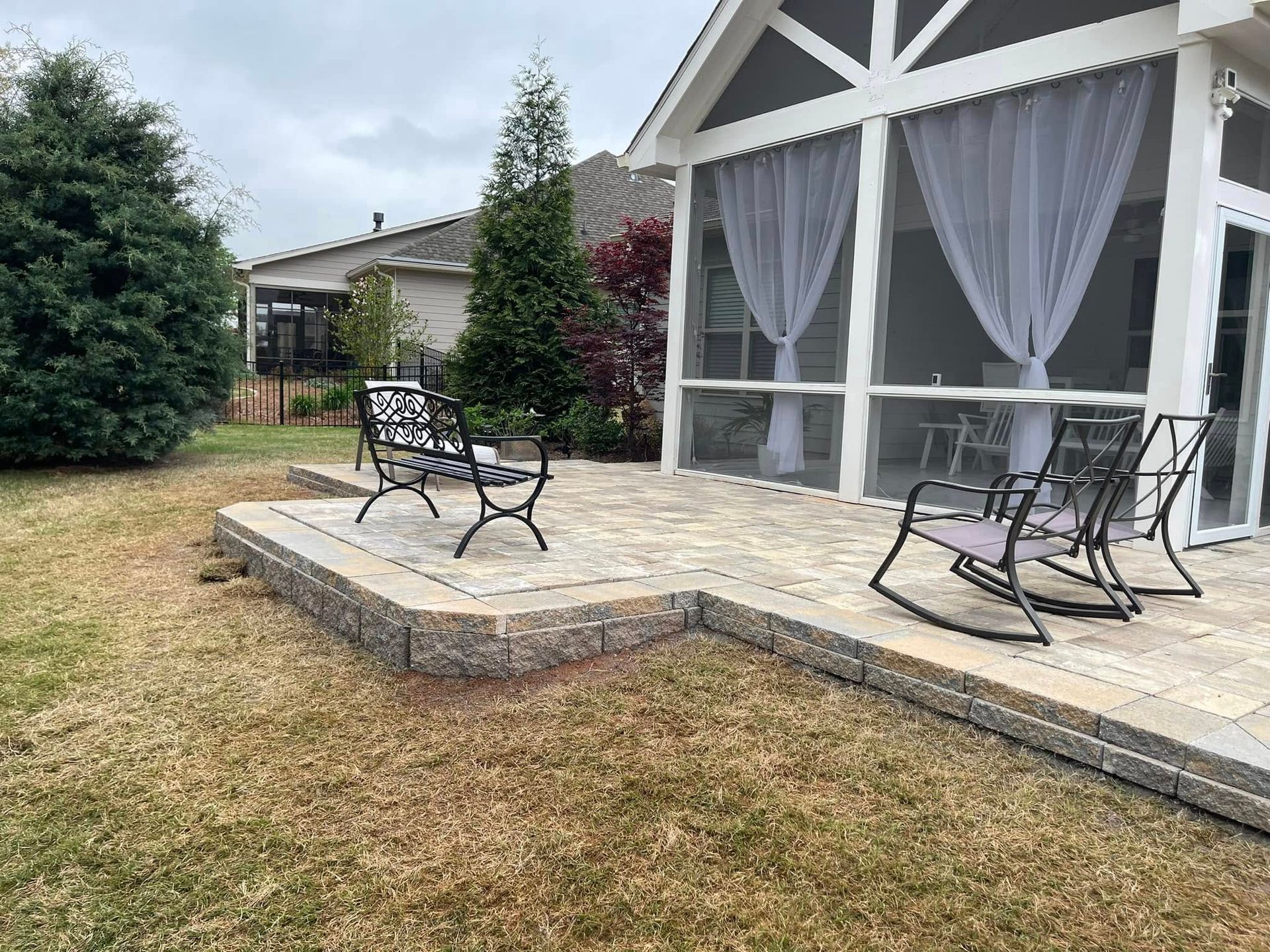 Patio with black metal chairs and table beside a screened porch and stone steps in a dry yard