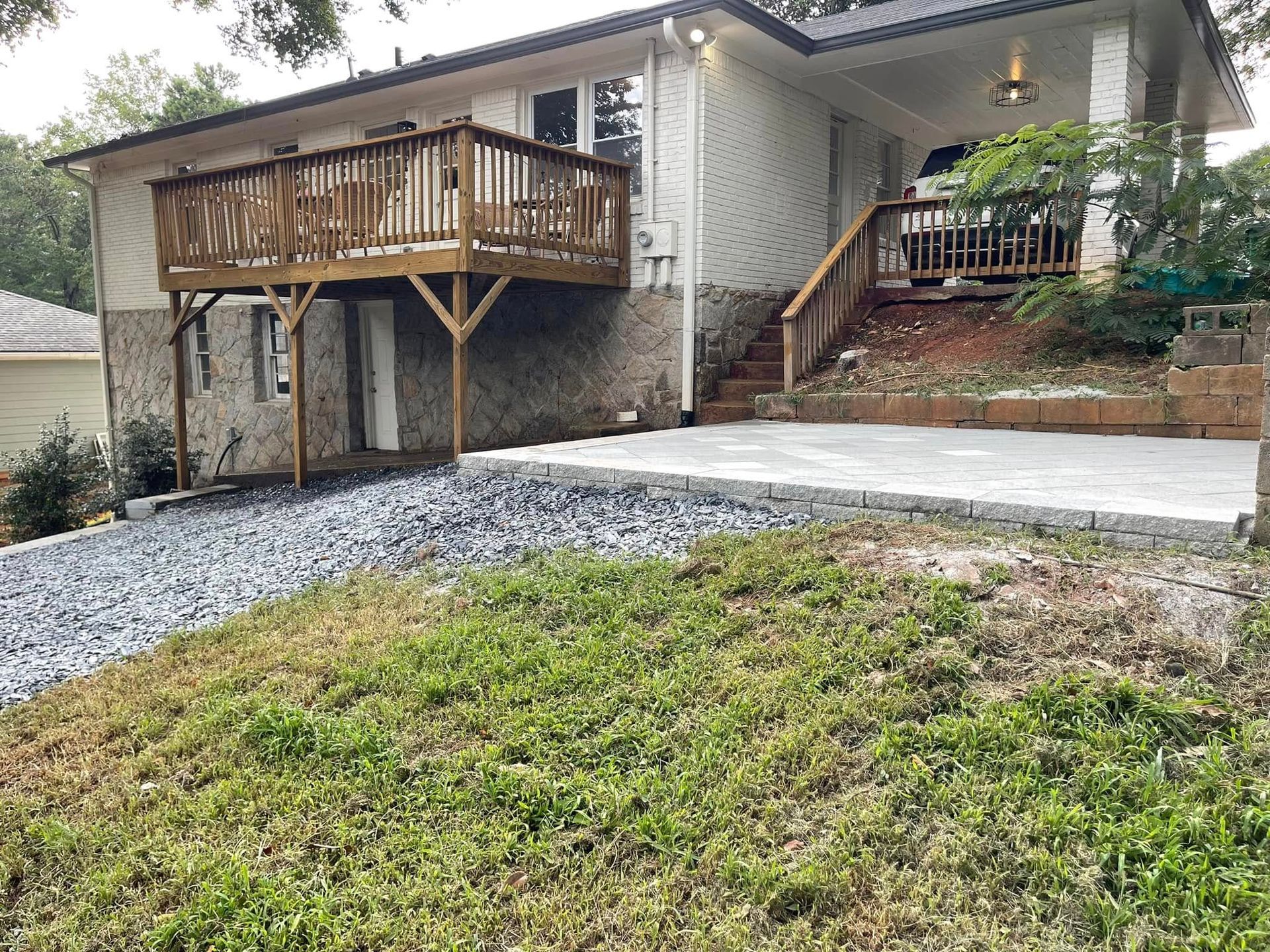 House exterior with wooden deck, concrete driveway, and sloped gravel-and-grass front yard