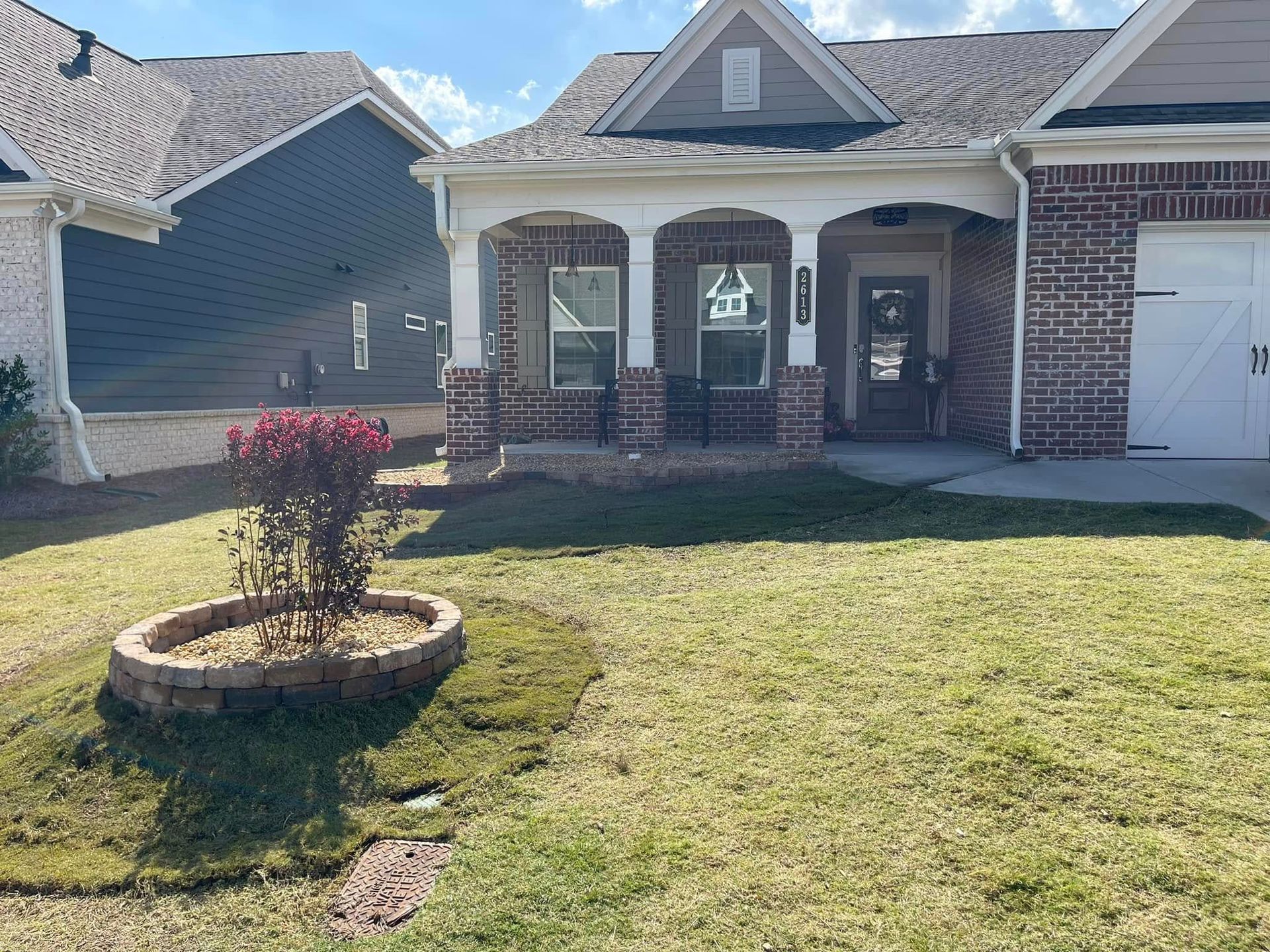 Suburban brick house with covered porch and a small landscaped front yard, including a circular flower bed.