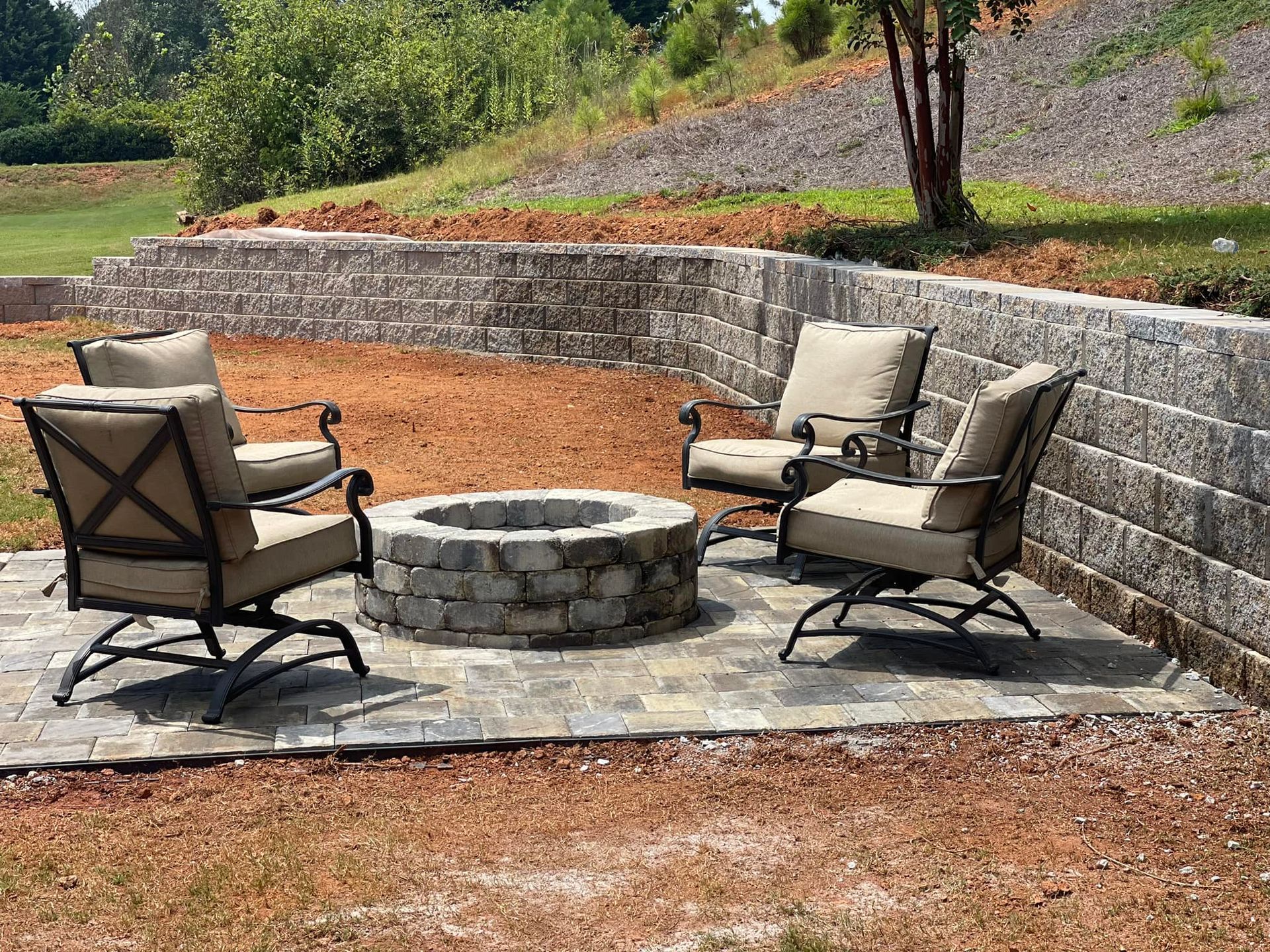 Three patio chairs around a stone fire pit on a paved backyard terrace