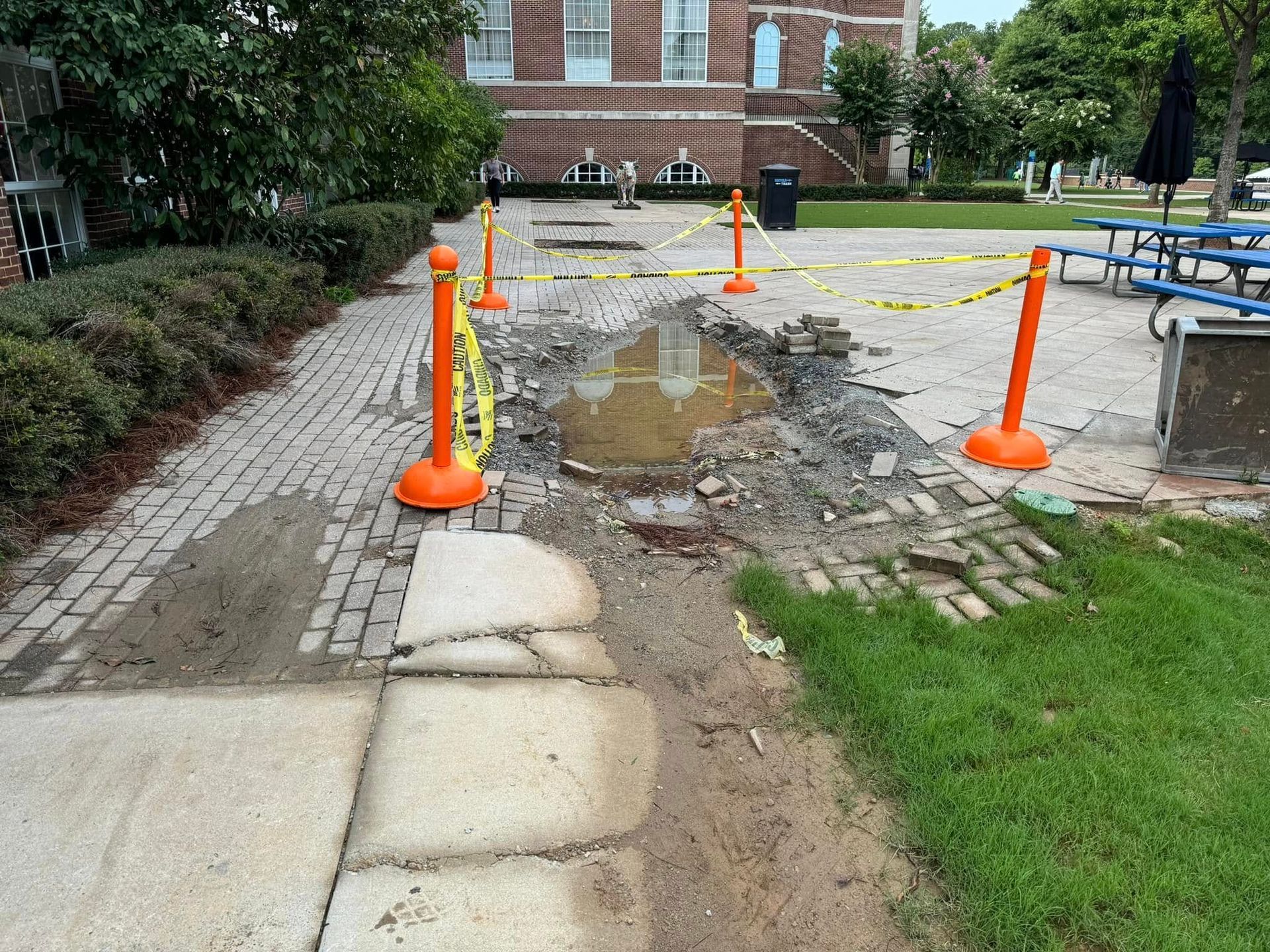 Blocked walkway with standing water and orange cones outside a brick building