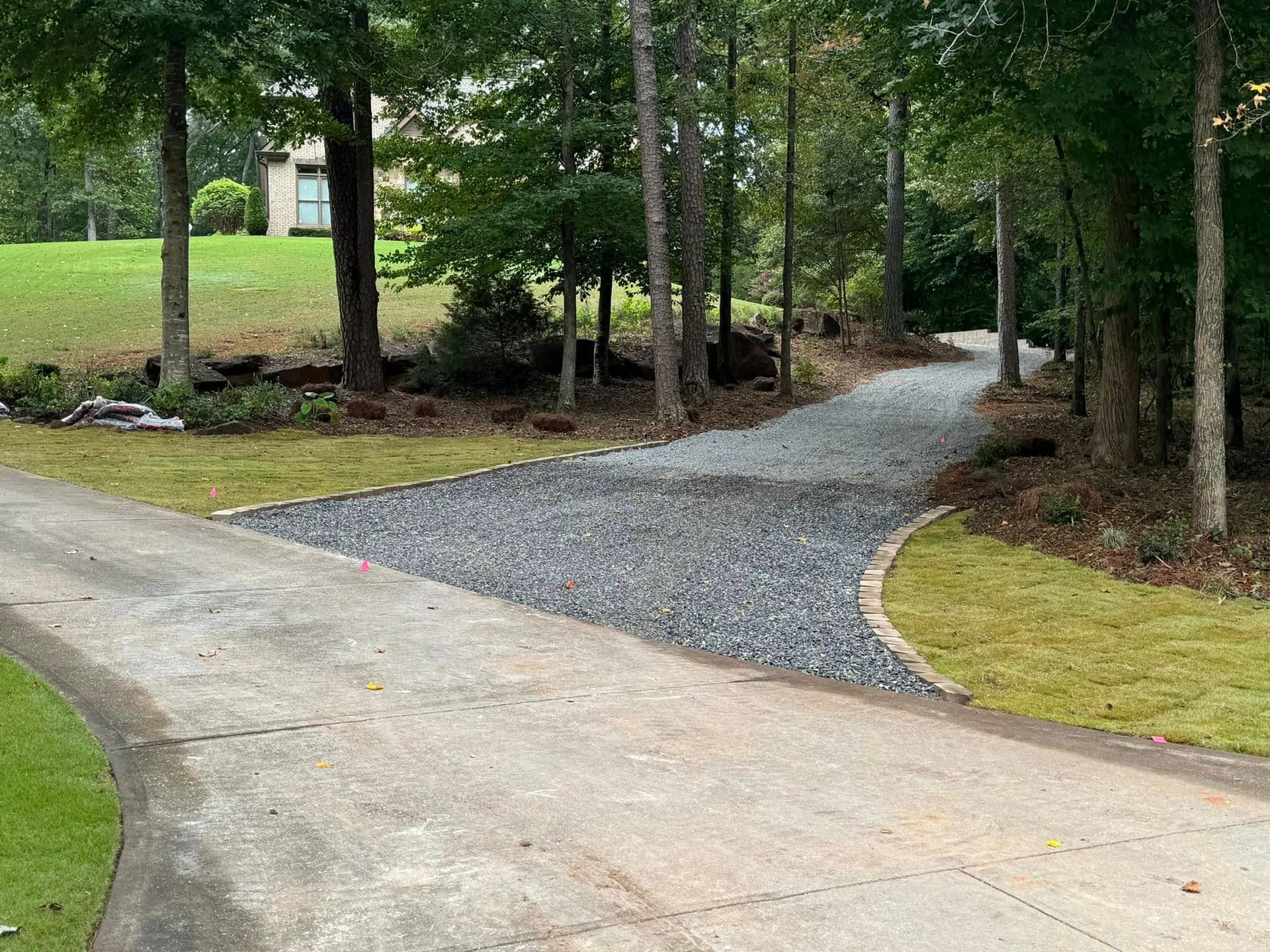 Curving gravel driveway through a wooded yard with grass and trees