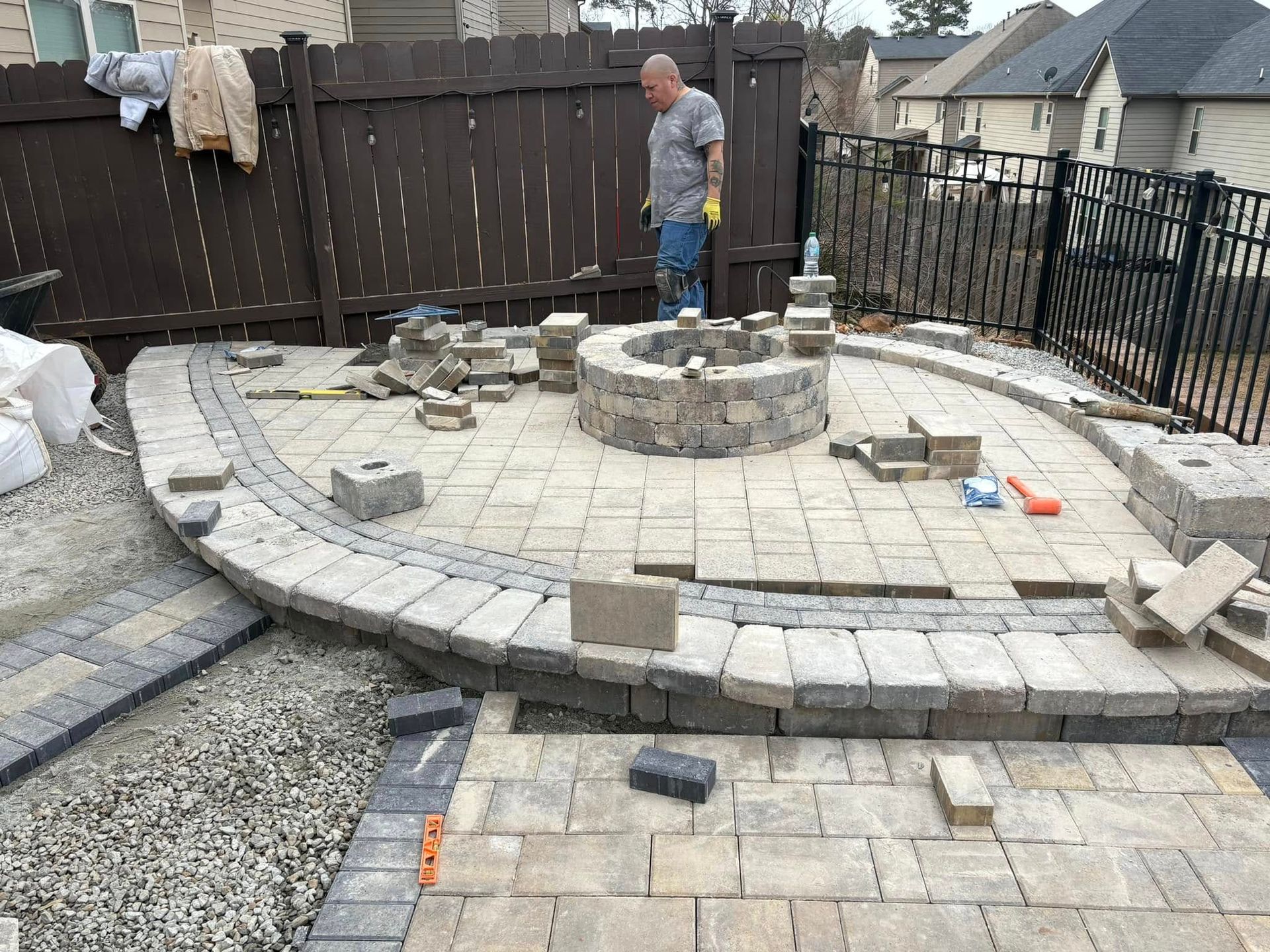 Stone patio under construction with a circular raised fire pit and a worker standing in the center