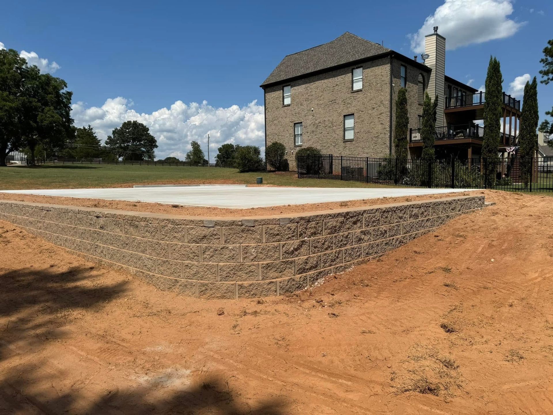 Stone house beside a newly built gravel and concrete patio under a blue sky