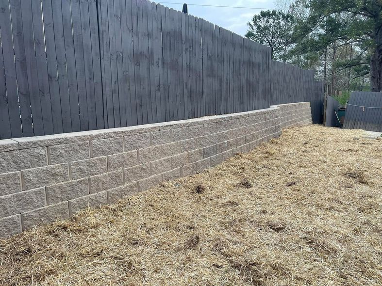 Backyard with tan retaining wall, dark privacy fence, and mulch-covered slope