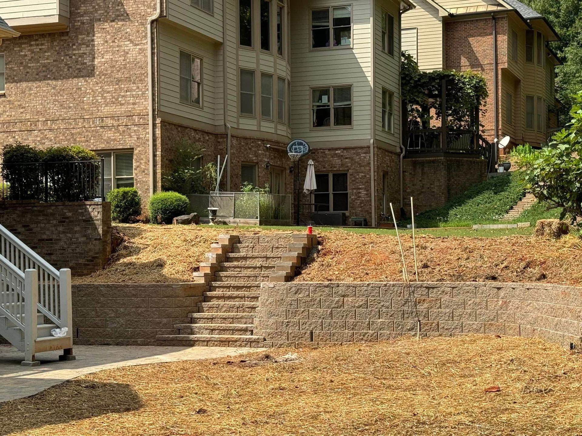 Brick apartment courtyard with stone steps, retaining walls, and dry grass under trees