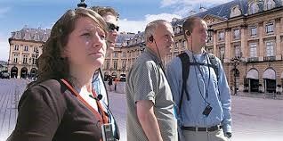 Group of people on a walking tour, using audio guides, in front of a building.