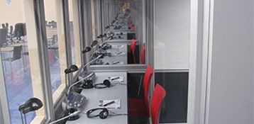 Rows of workstations with headsets and red chairs, likely a control room or office setting.