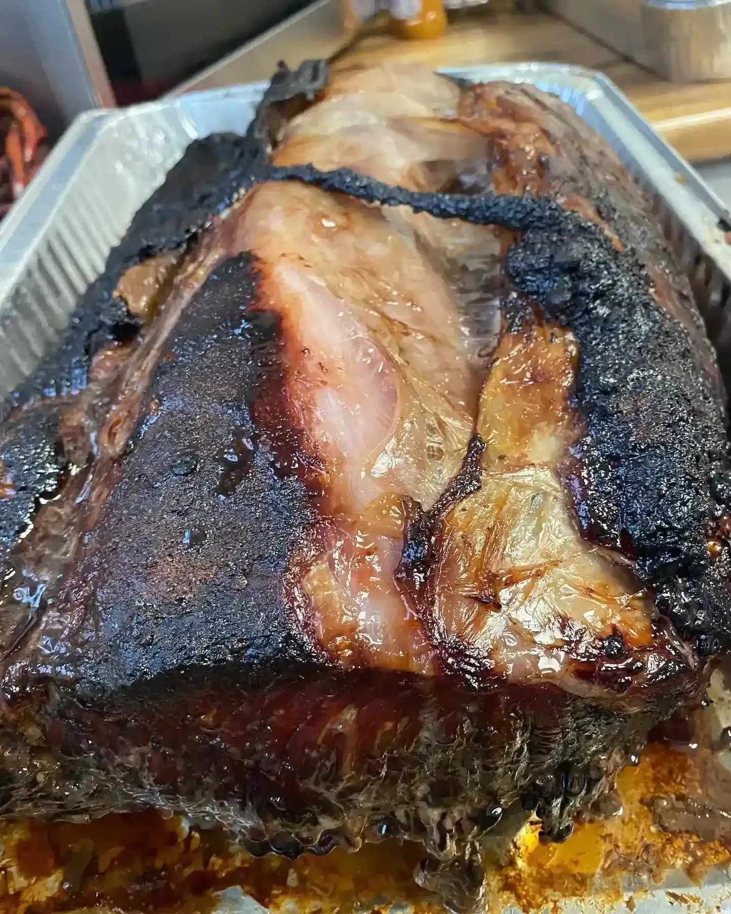 Charred smoked brisket in a foil tray, with a dark bark and visible juicy slices underneath