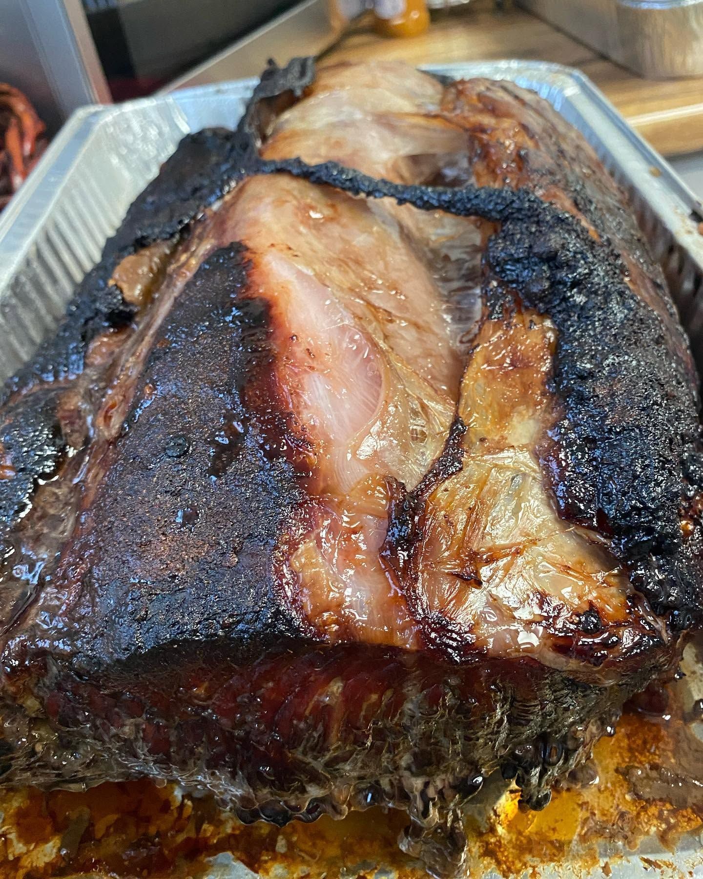 Charred smoked brisket in a foil tray, with a dark crust and visible juices
