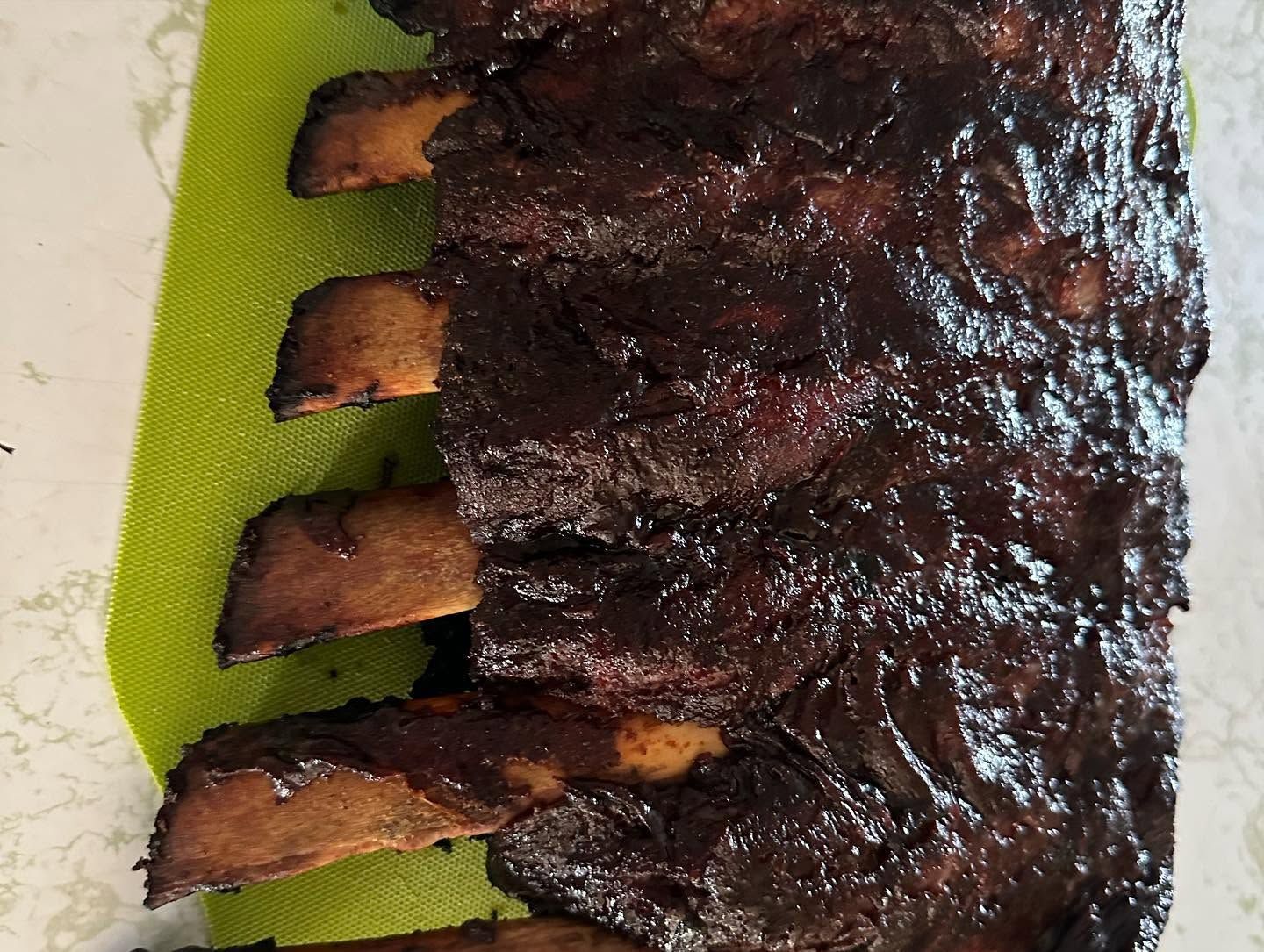 Close-up of a glazed rack of barbecued ribs on a green cutting board.