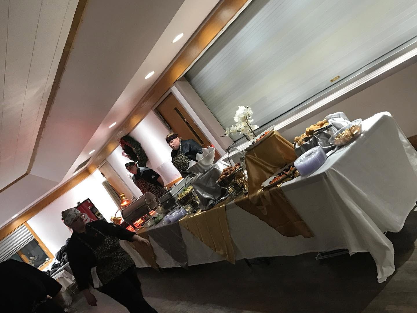 Buffet tables in a banquet hall with food trays and a few people serving themselves