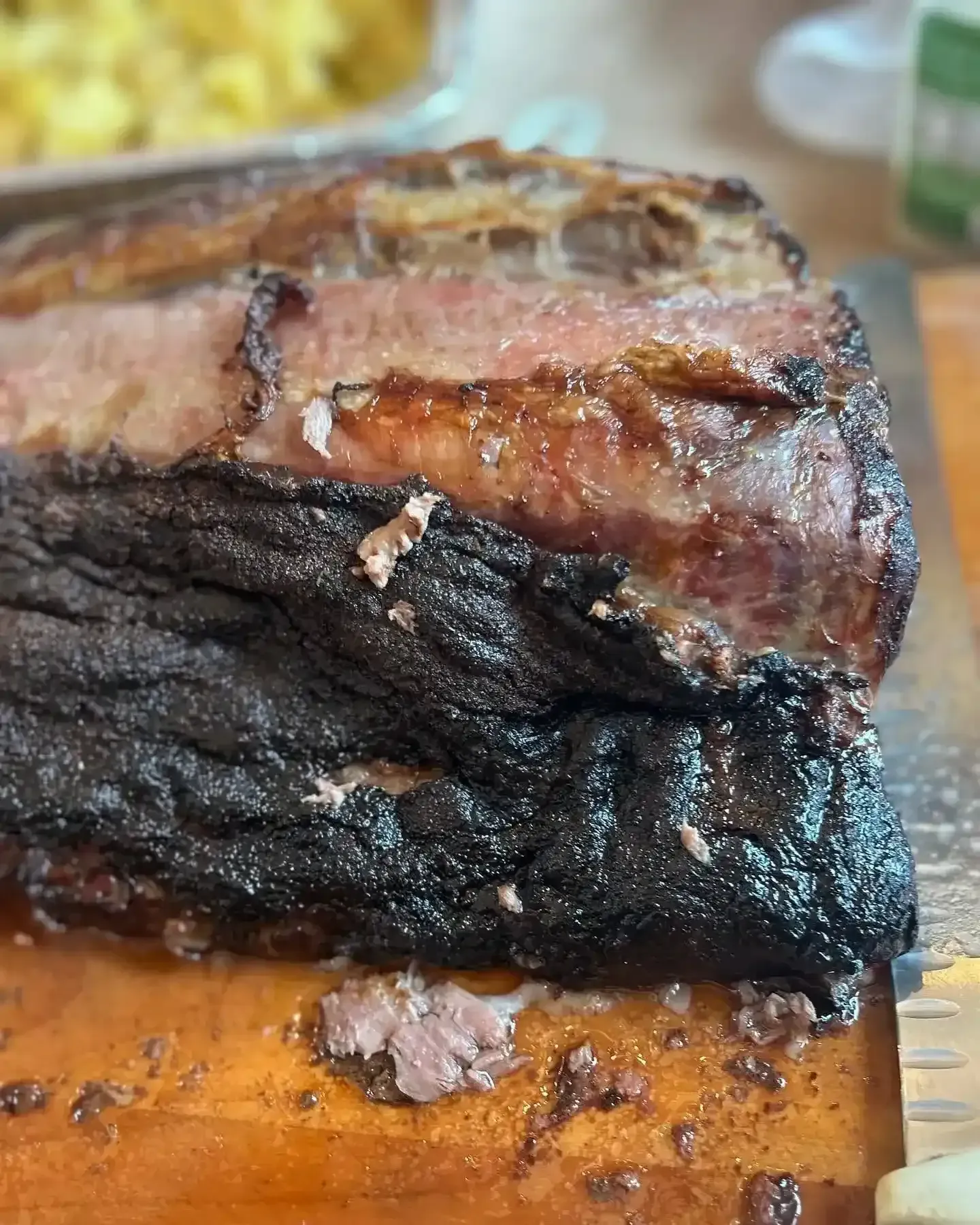 Close-up of a charred, smoked meat roast on a cutting board, with a browned crust and juicy center.