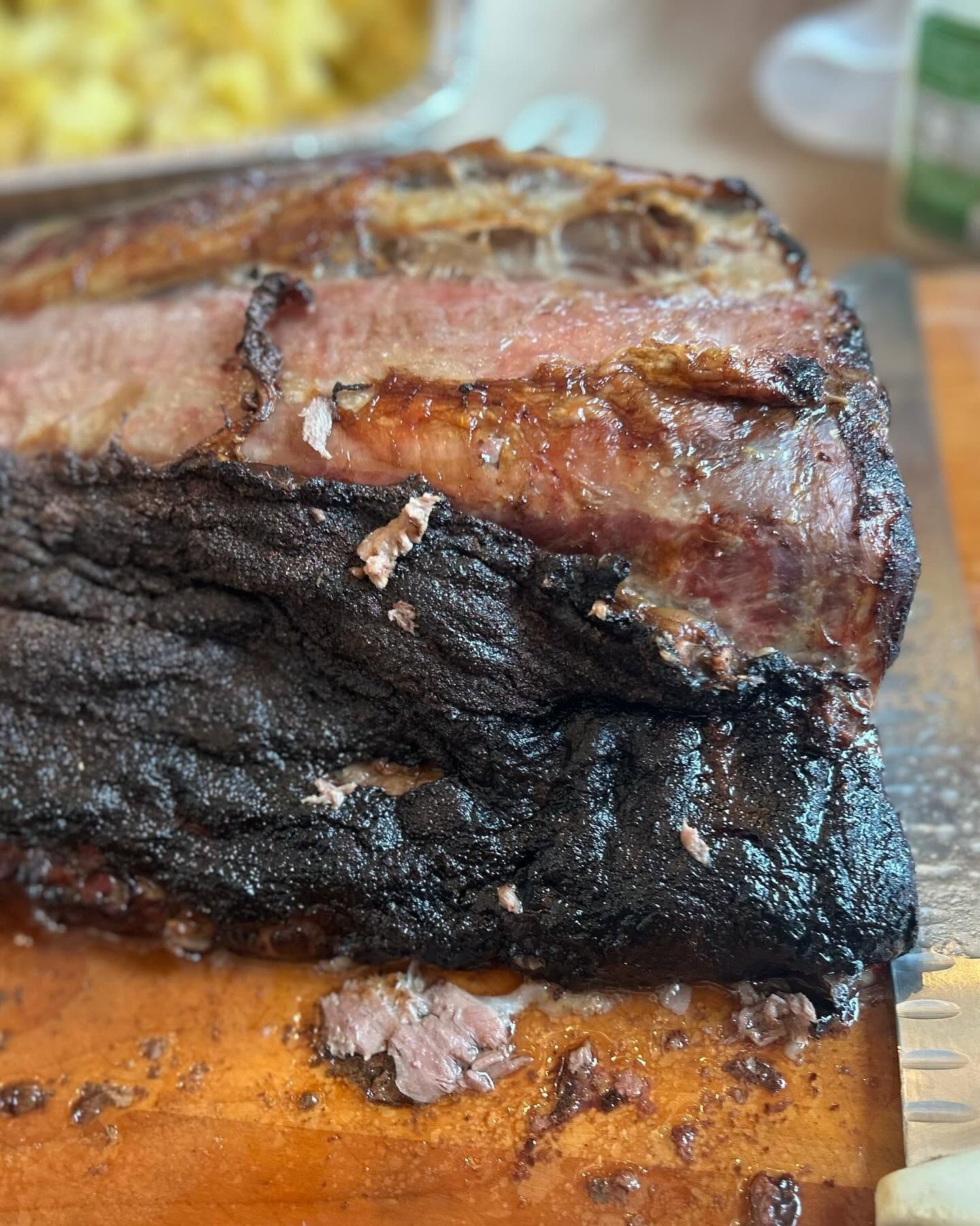 Close-up of a charred, smoked meat roast on a cutting board, with a browned crust and juicy center.