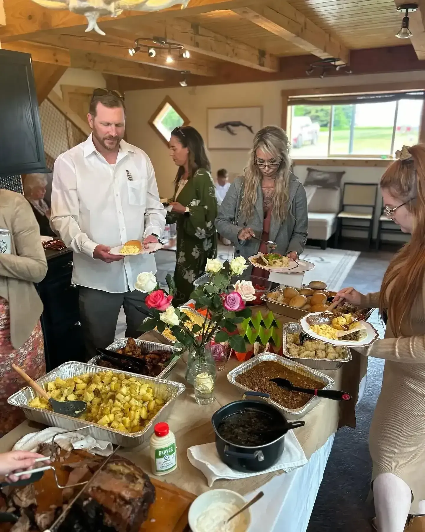 People serving themselves at a buffet table with flowers in a bright rustic dining hall