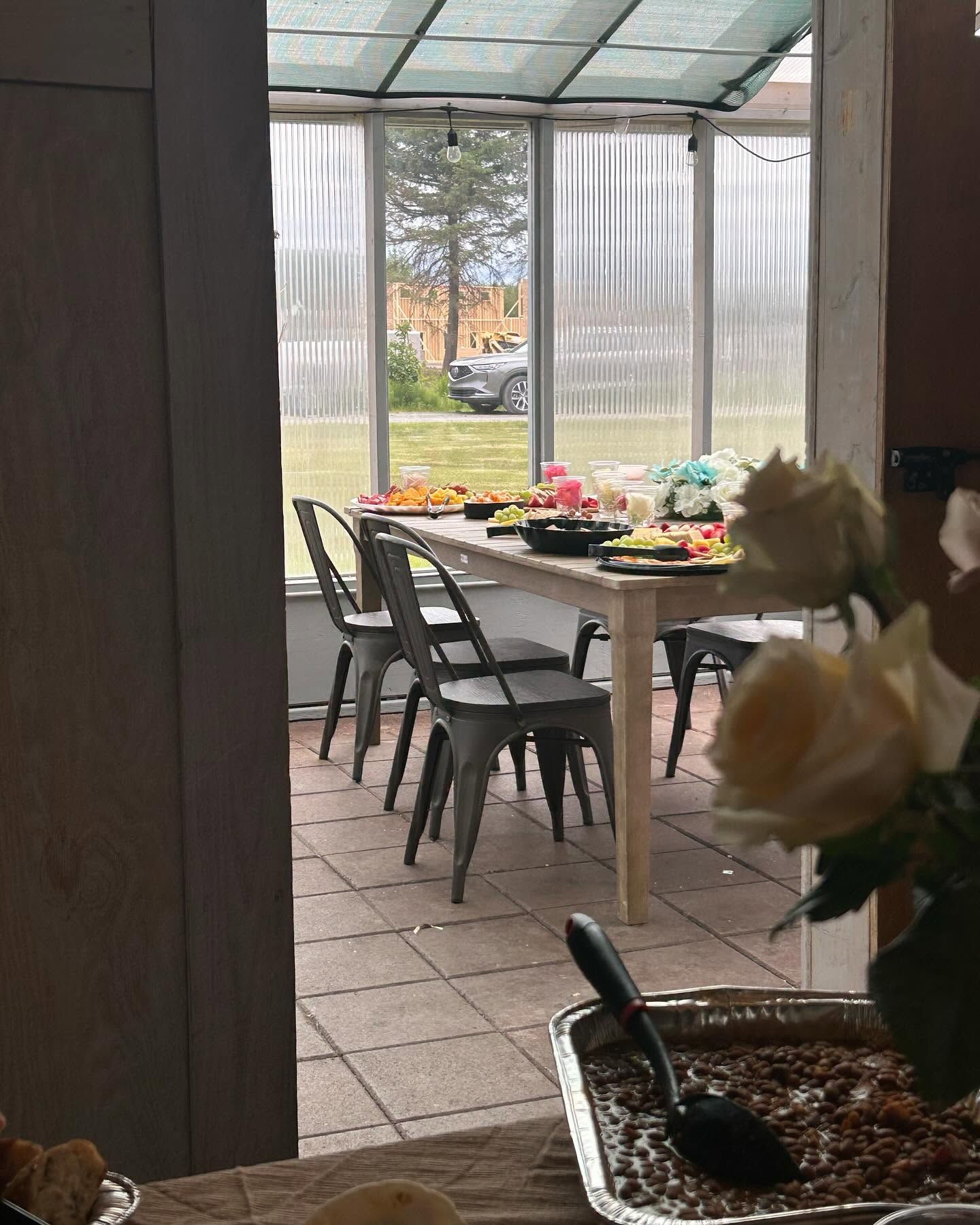 Covered patio with a table set for a meal, chairs, and flowers in the foreground, overlooking a yard.