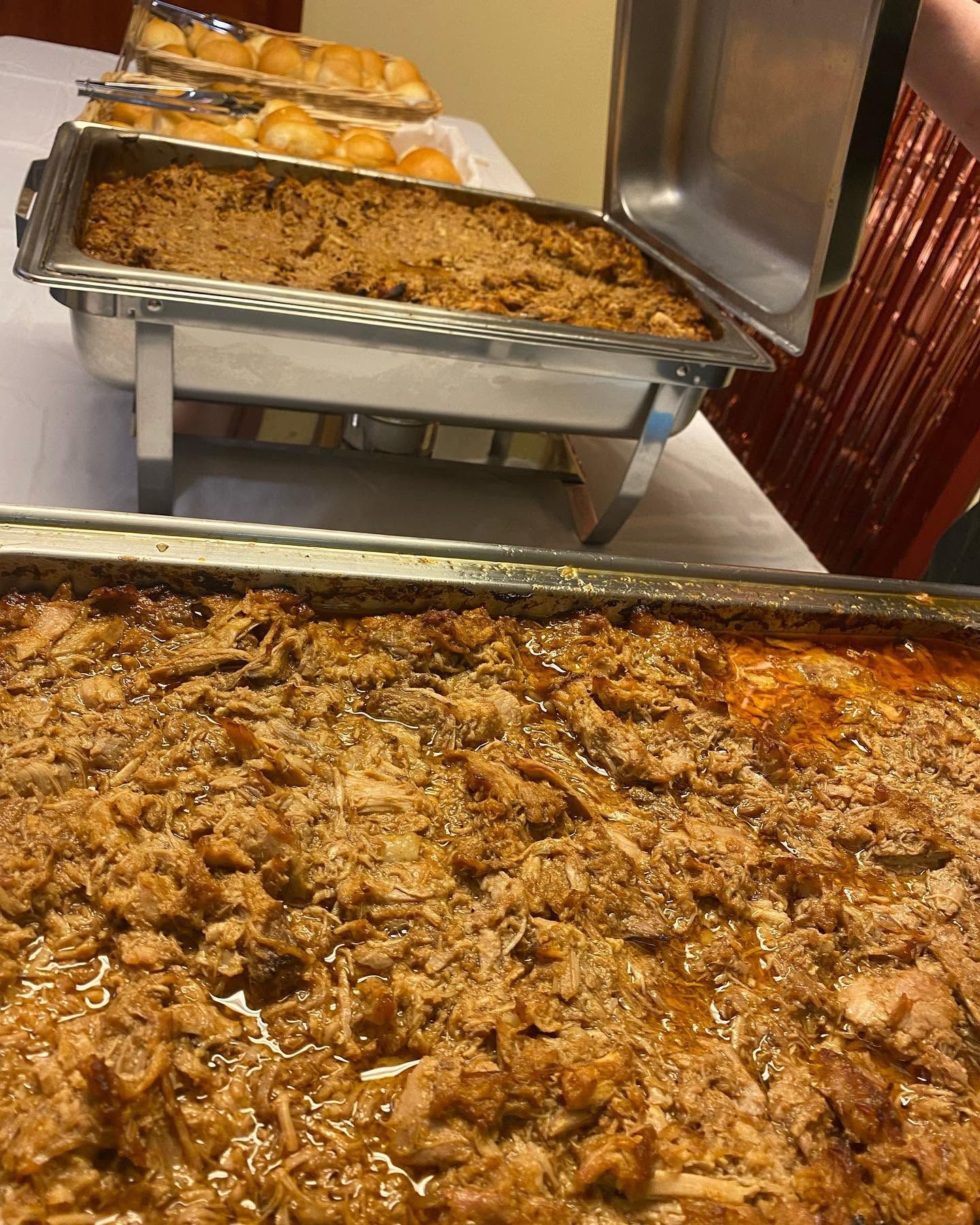 Tray of baked pasta or casserole at a buffet, with a warm-brown topping and rolls in the background