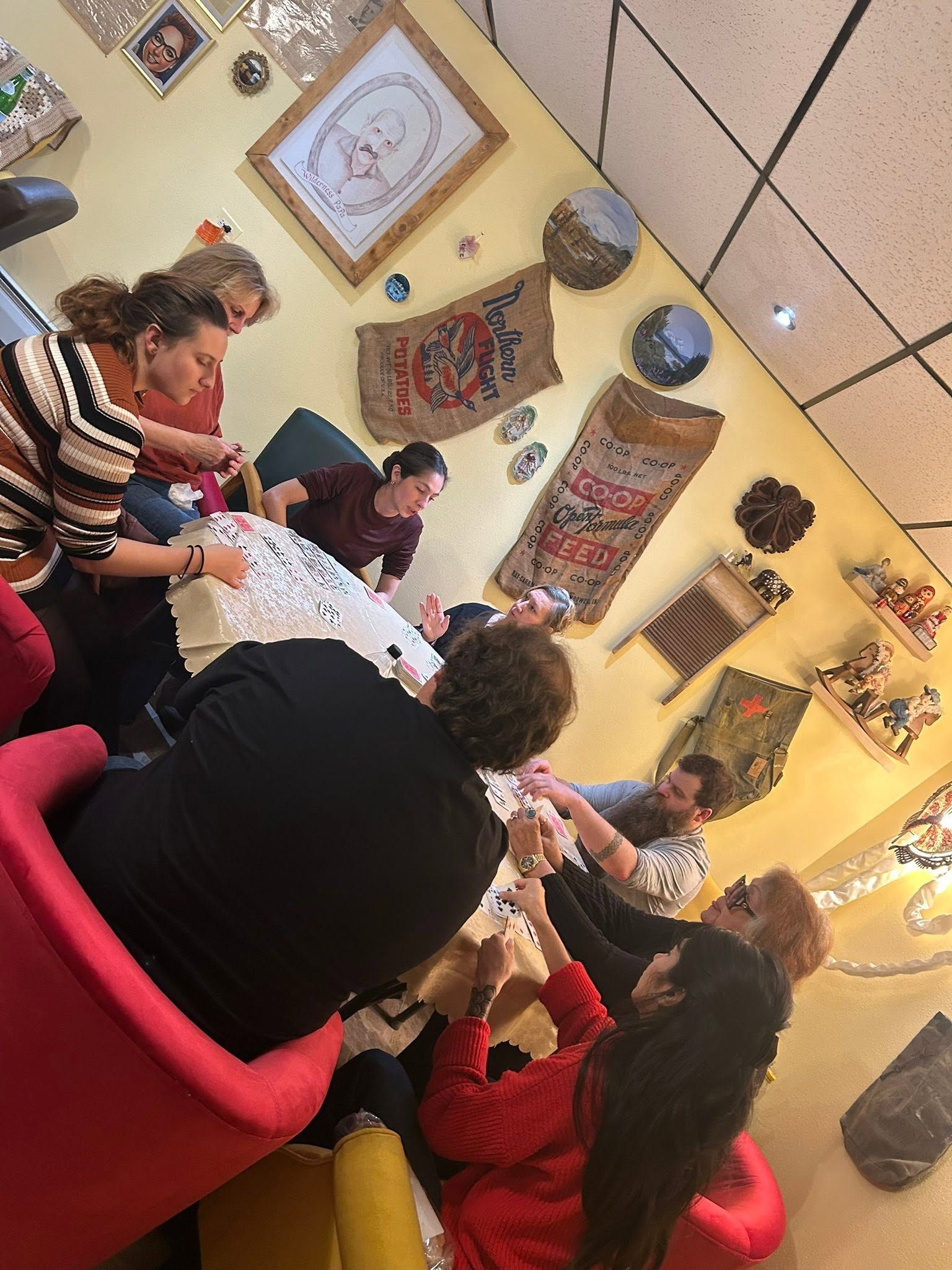 People seated around a table in a cozy cafe, chatting under wall art and warm lighting.