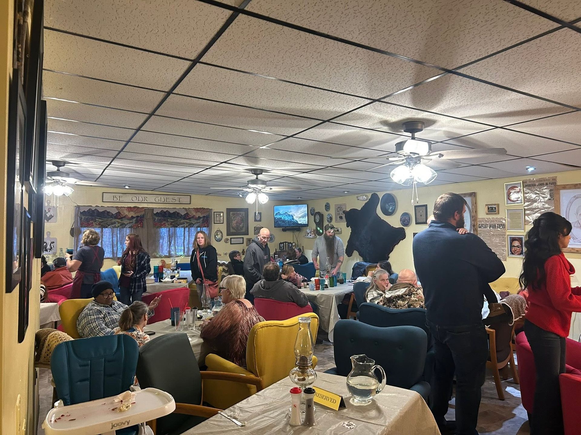 Crowded restaurant with people dining and mingling under bright ceiling lights, tables and chairs throughout