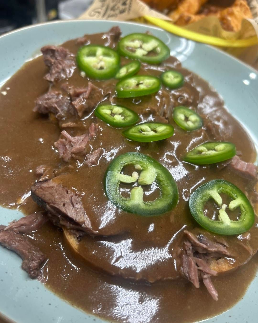 Braised meat in brown gravy topped with sliced green jalapeños on a blue plate