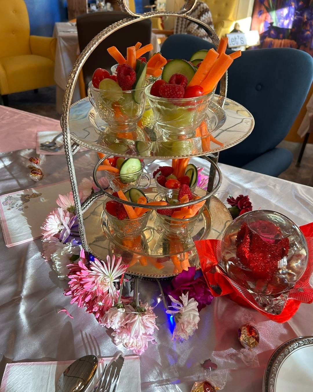 Three-tier dessert stand with fruit-topped treats and red glass ornaments on a festive table.
