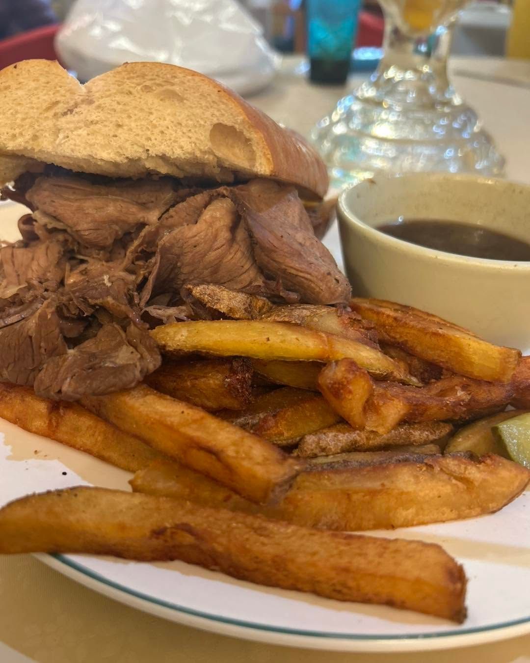 Sandwich with roast meat and fries on a plate, with dipping sauce on the side.