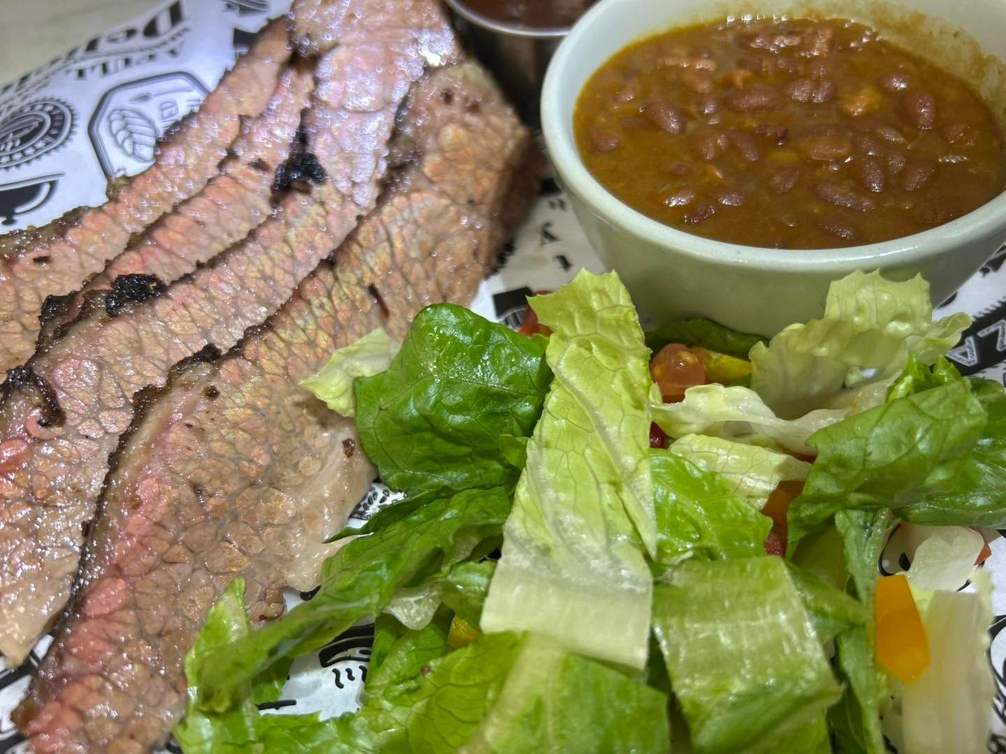 Sliced steak, baked beans, and a green salad on a plate