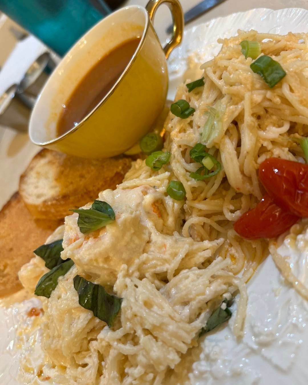Creamy pasta on a white plate with basil, cherry tomatoes, and a small yellow cup of sauce.