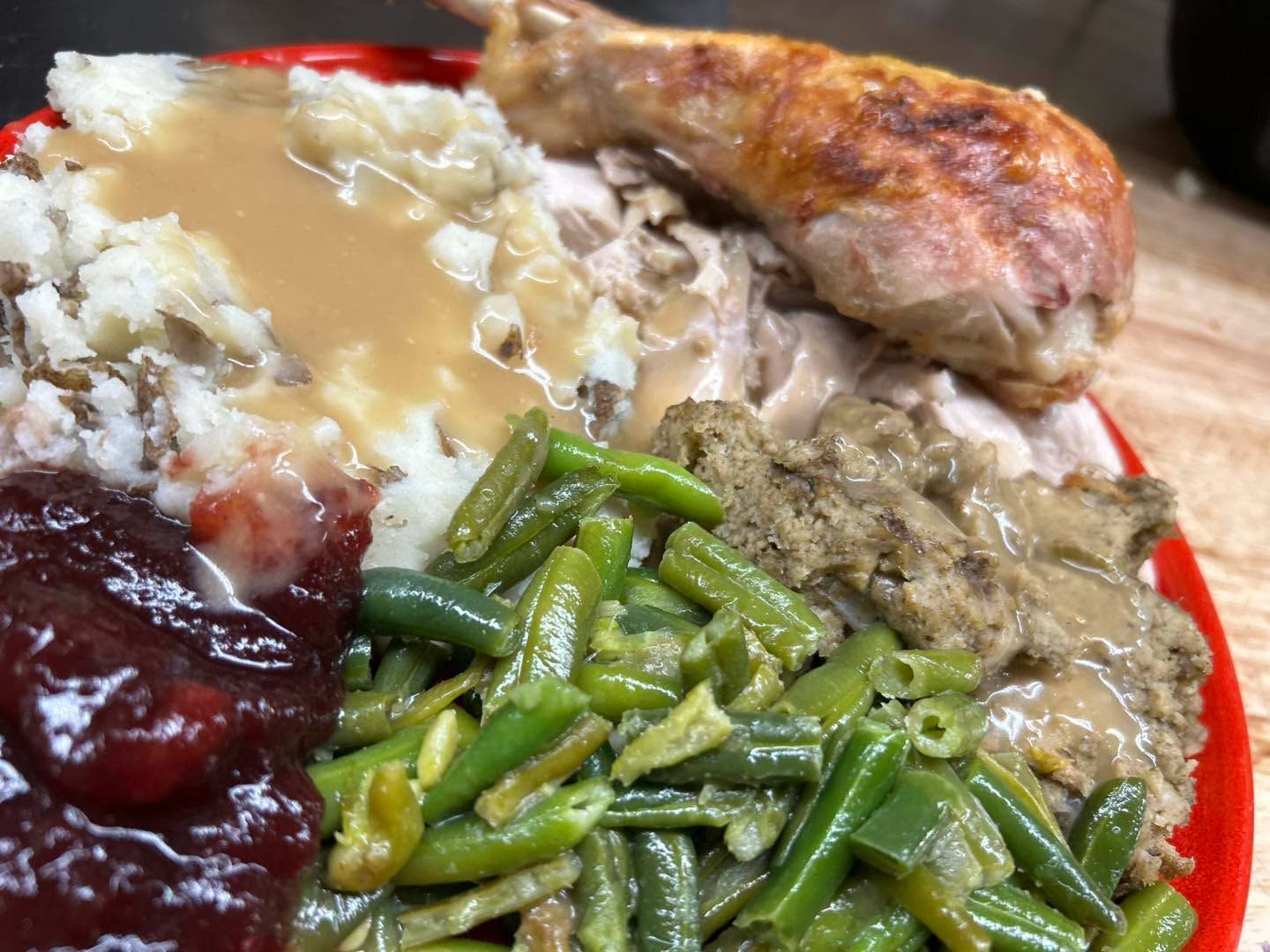 Plate of roasted chicken with gravy, green beans, mashed potatoes, and cranberry sauce on a red rimmed dish