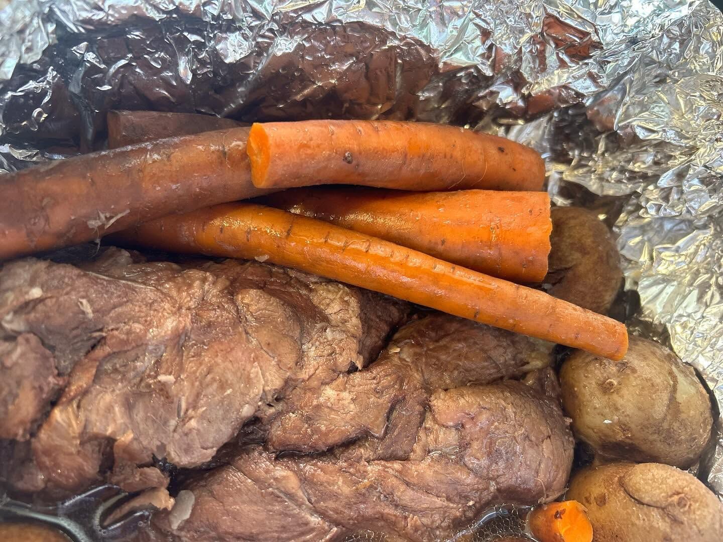 Brown roasted meat with carrots and potatoes in foil package