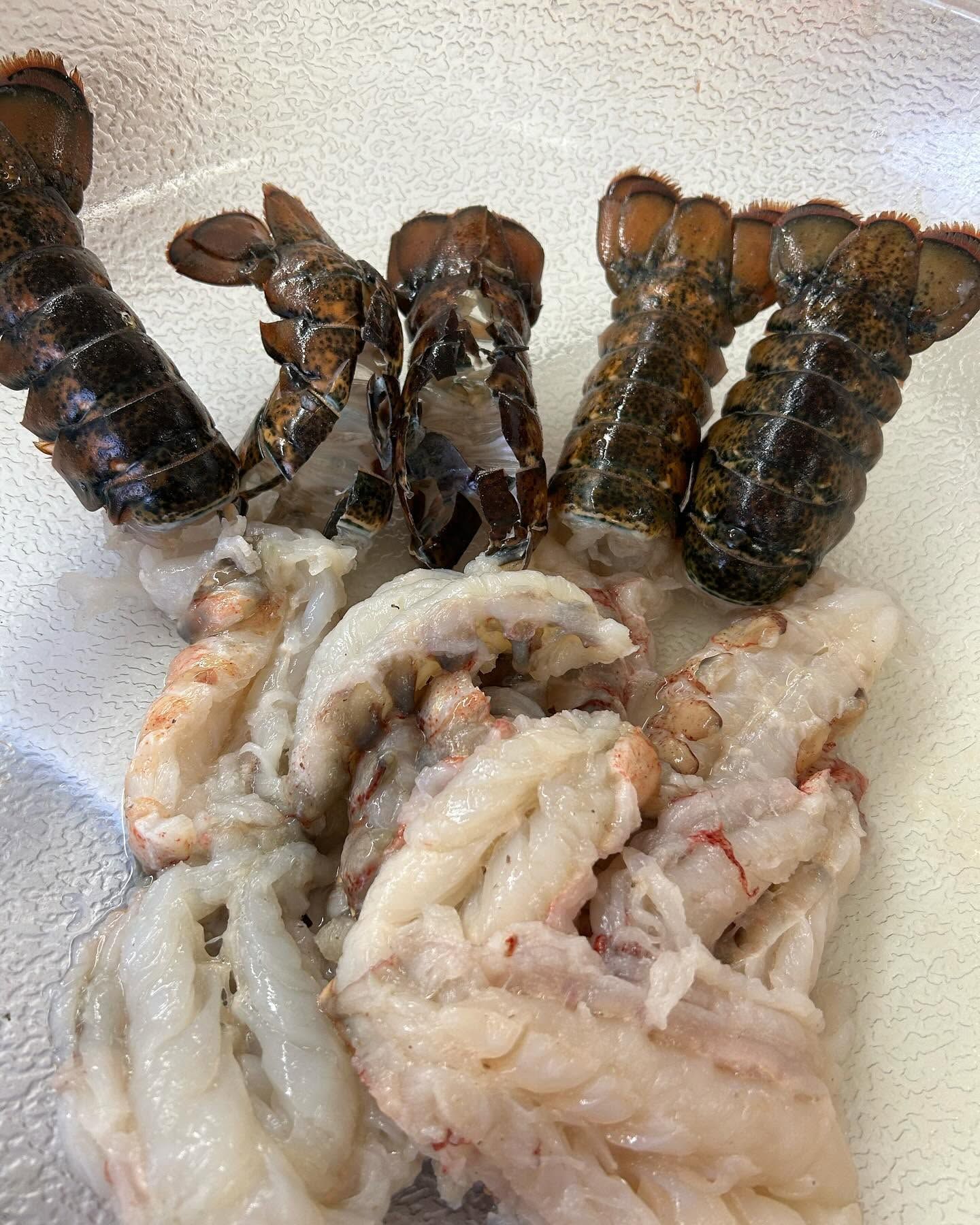 Raw lobster tails on a plate, with dark shells and pale lobster meat displayed side by side