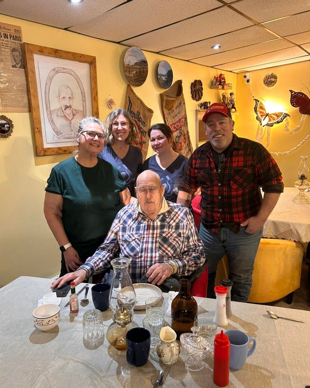 Five people smiling at a table in a warmly lit restaurant with yellow walls and artwork.