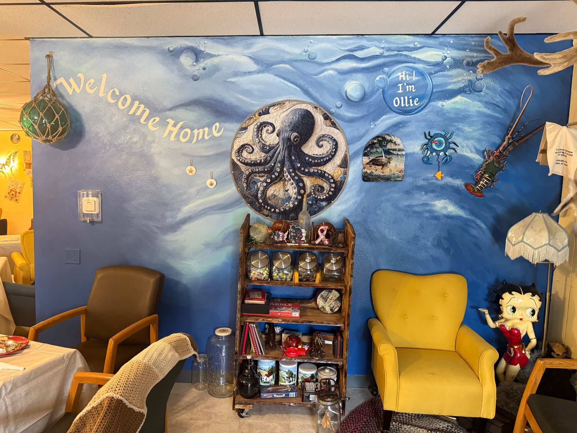 Mural-painted waiting area with chairs, a yellow armchair, shelf, and ocean-themed wall art