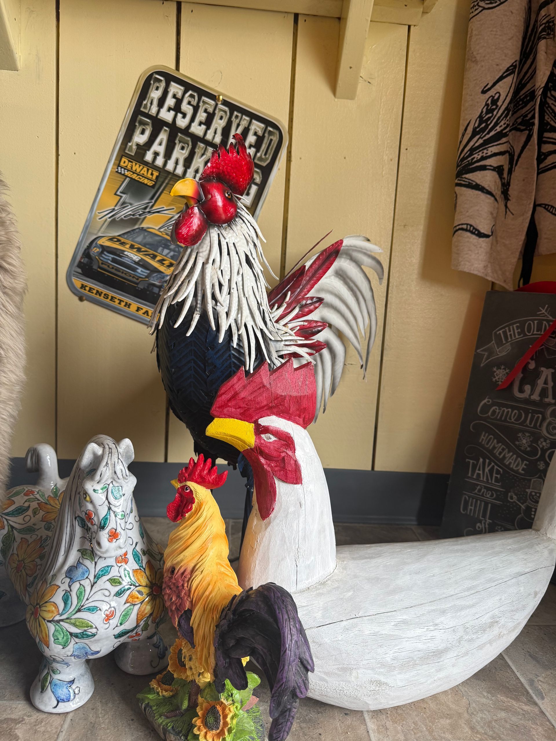 Rooster figurines beside a porch sign that reads “Reserved Parking,” with a painted wooden wall behind.