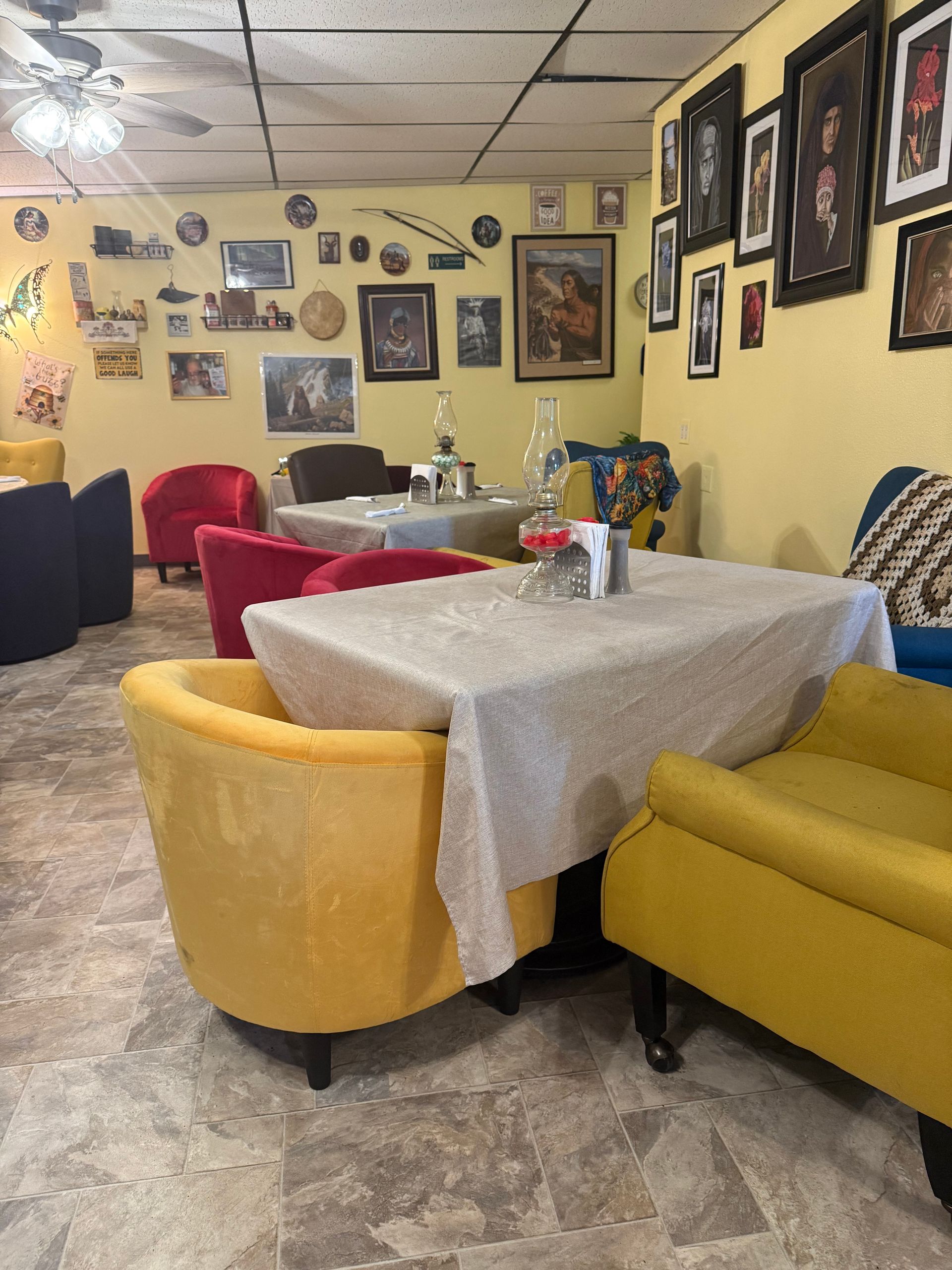 Cozy restaurant seating area with yellow chairs, red seats, checkered tablecloths, and wall art