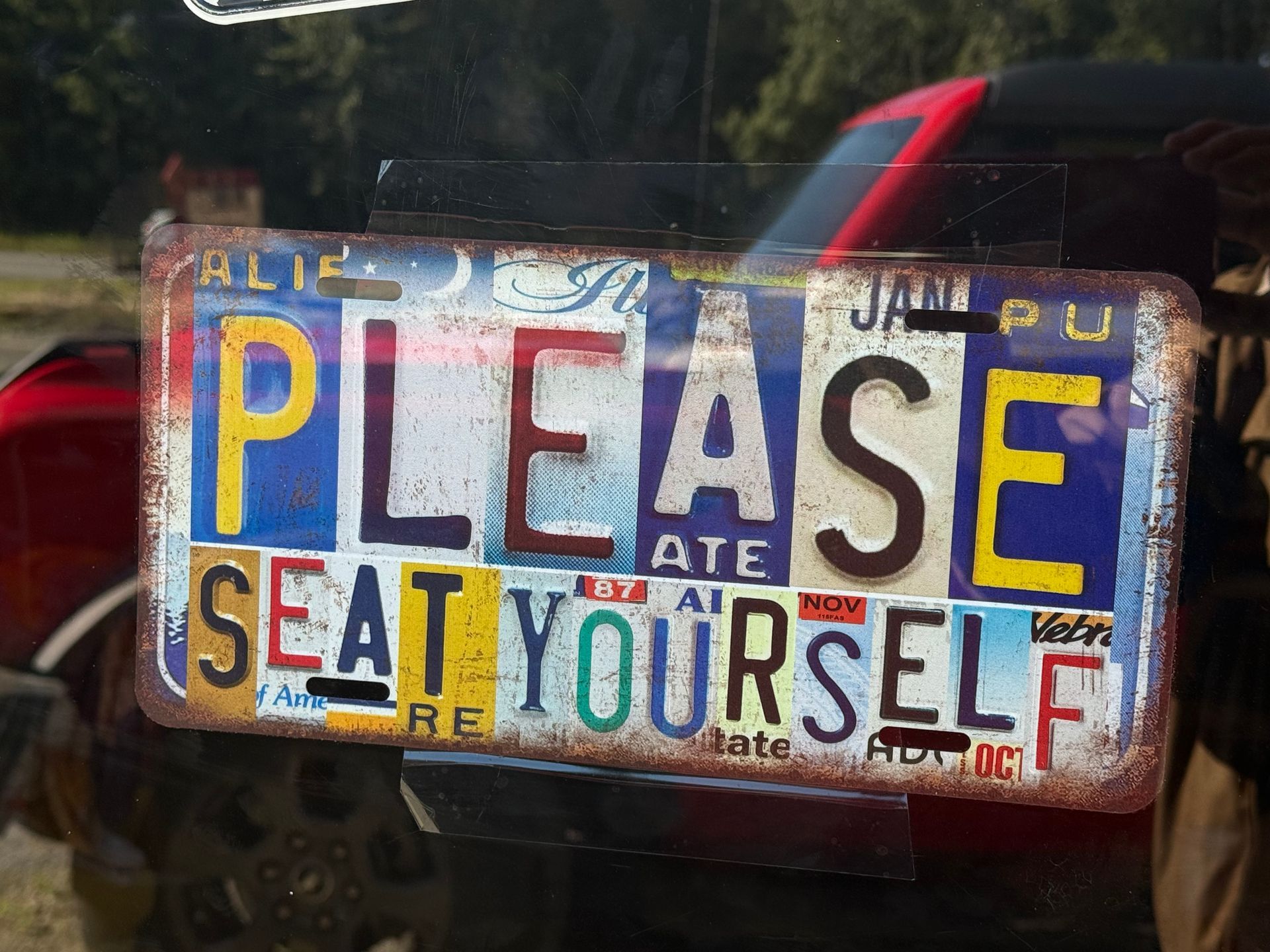 Colorful sign reading “PLEASE SEAT YOURSELF” with blue, white, and yellow lettering.