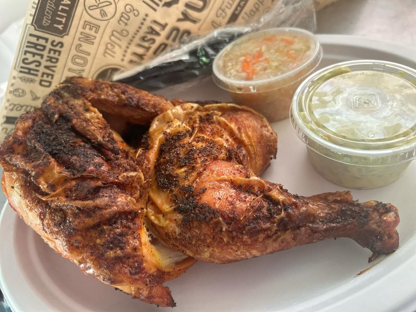 Grilled chicken leg quarter with two dipping sauces on a tray with newspaper-lined paper