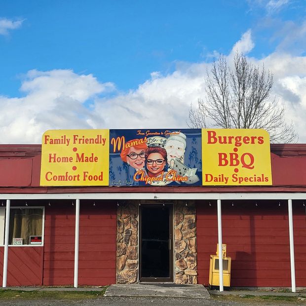 Red diner storefront with yellow signs for family-friendly home cooked food and burgers, BBQ, daily specials