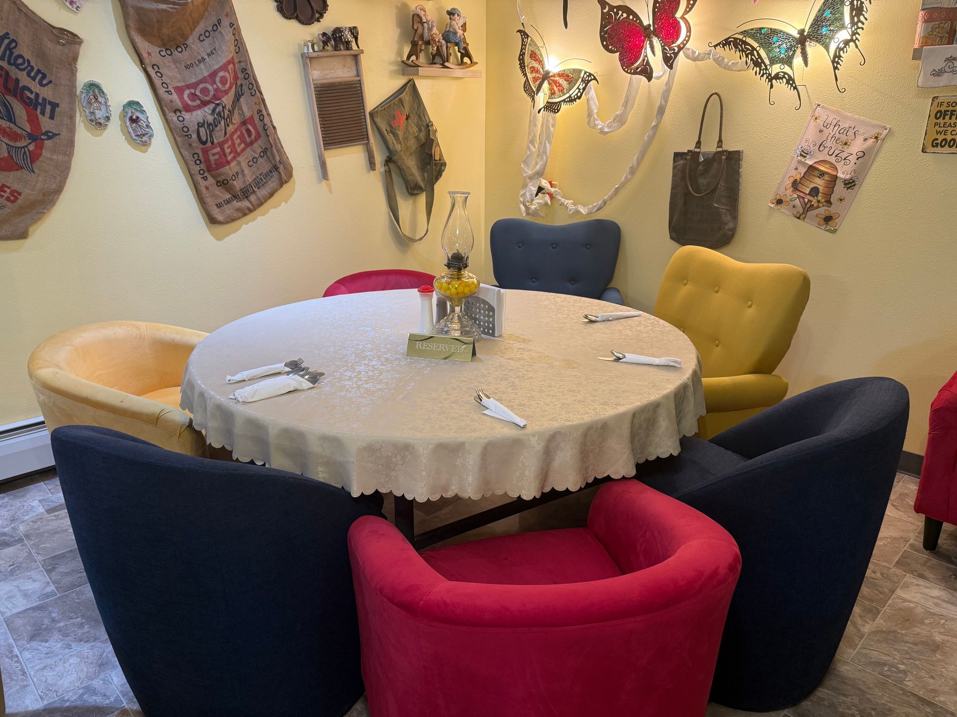 Colorful café seating with a round table, upholstered chairs, and wall art under warm string lights