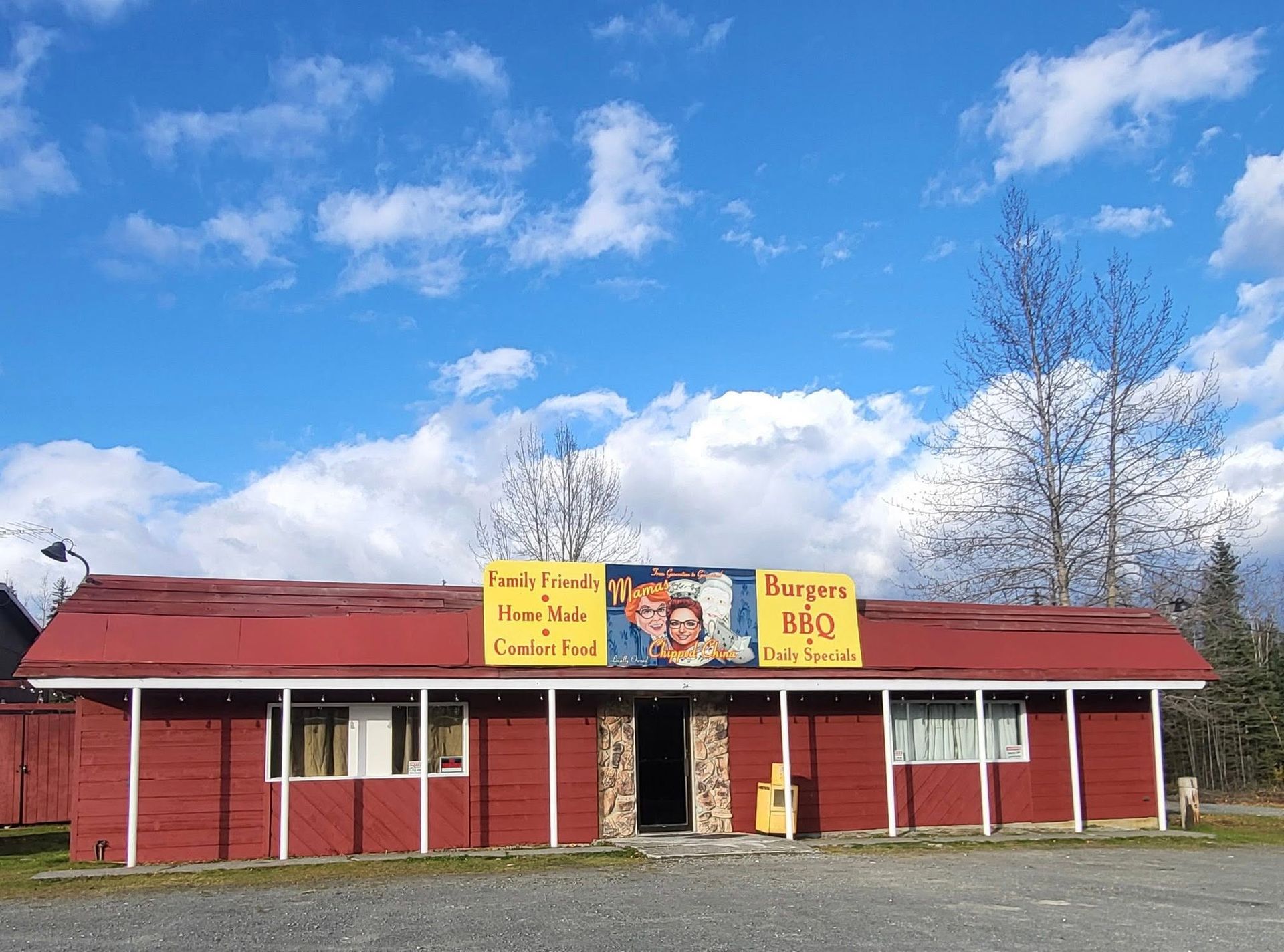 Red roadside market with yellow signs under a blue sky and clouds
