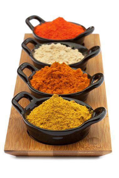 Four bowls of different spices are lined up on a wooden cutting board.