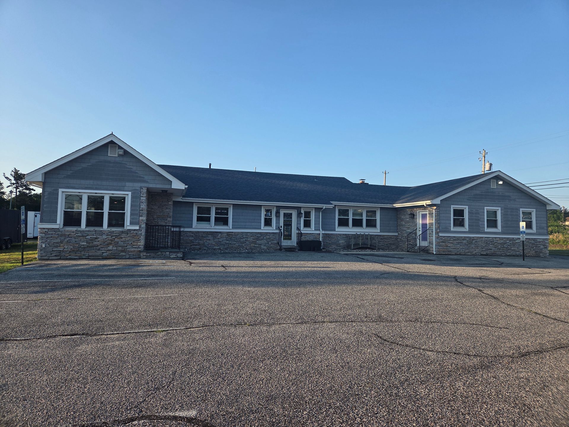 Single-story gray house with stone accents and a large gravel driveway under a clear blue sky