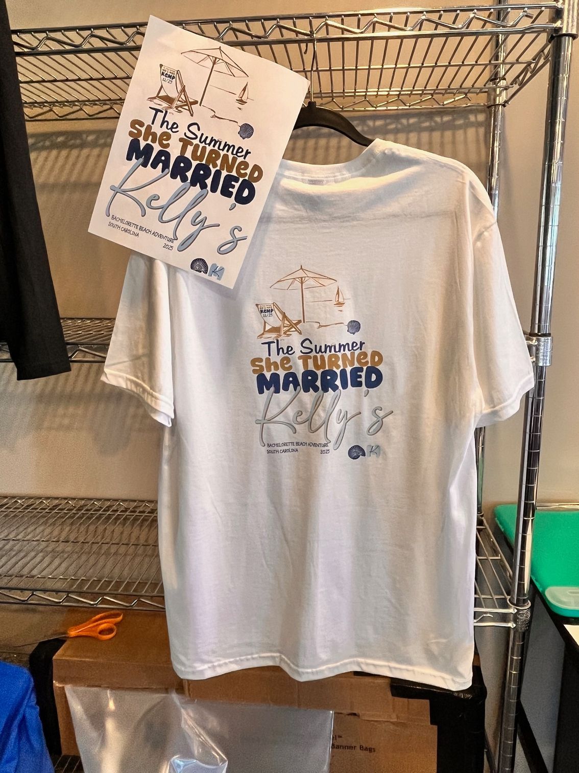White T-shirt with “The Quietly Married” design hanging on a clothing rack, with matching sign above.