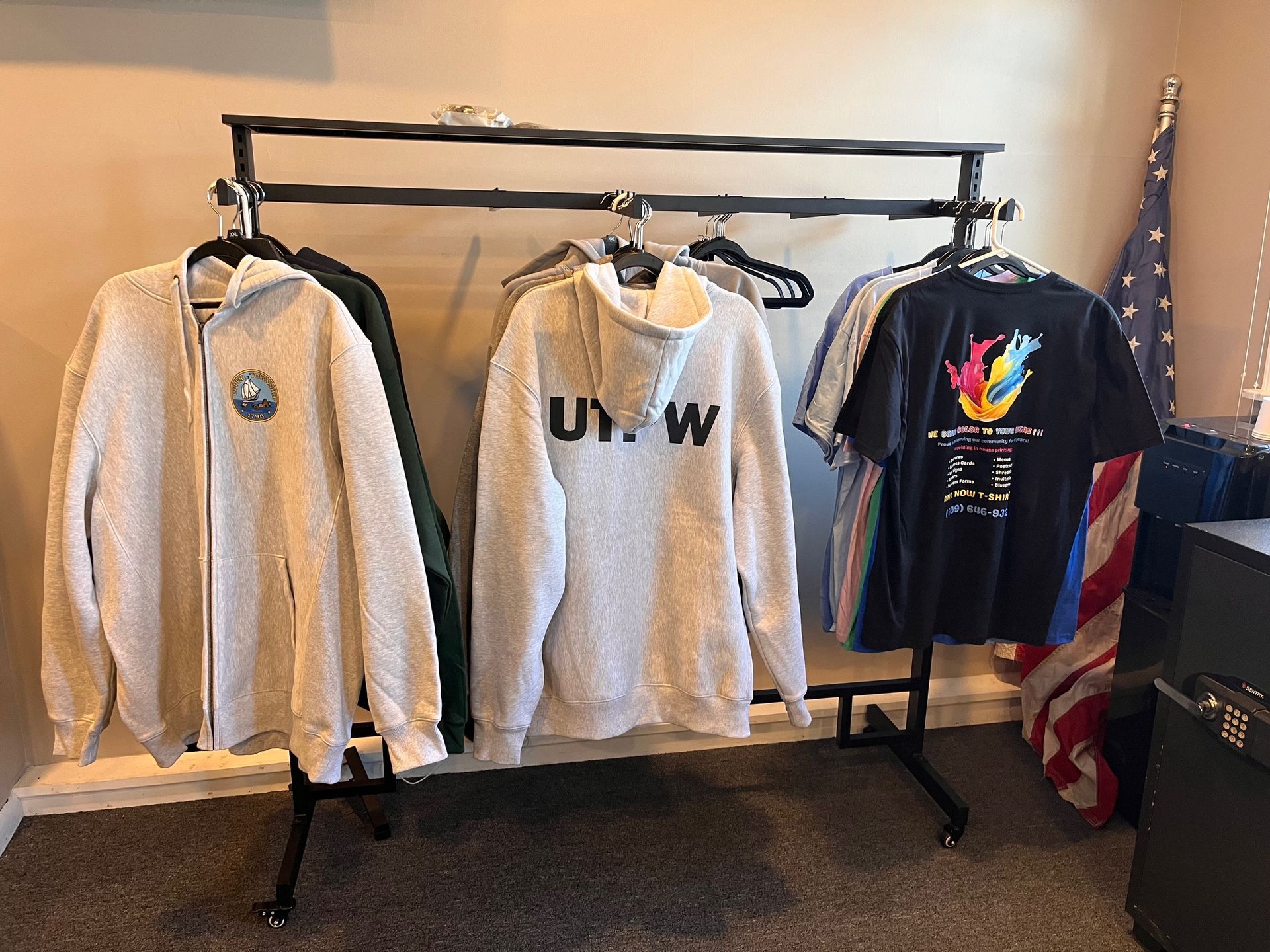 Clothing rack with beige and gray hoodies and a black graphic T-shirt in a room