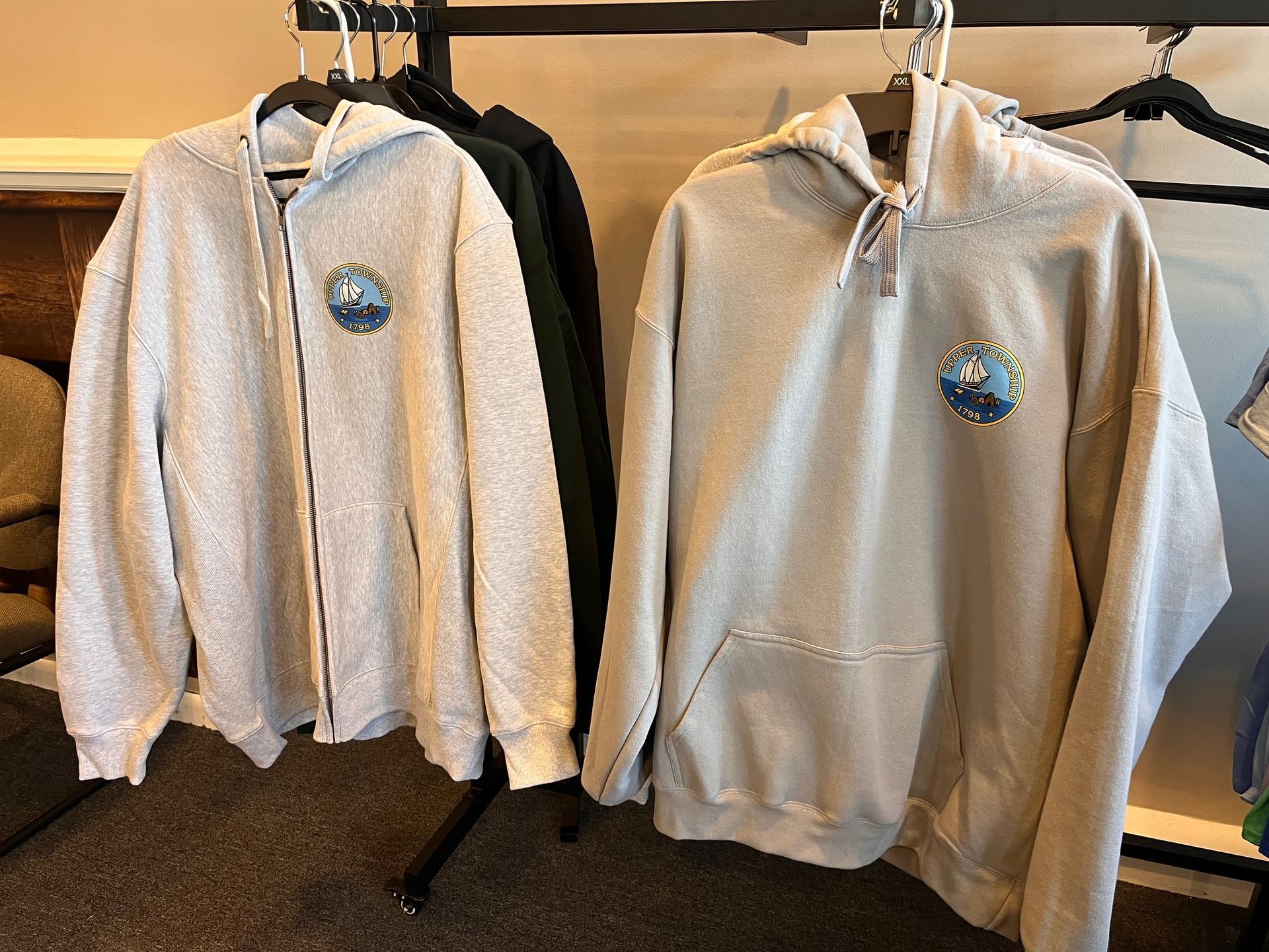 Two light-colored hoodies hanging on a clothing rack in a store, each with a small chest graphic.