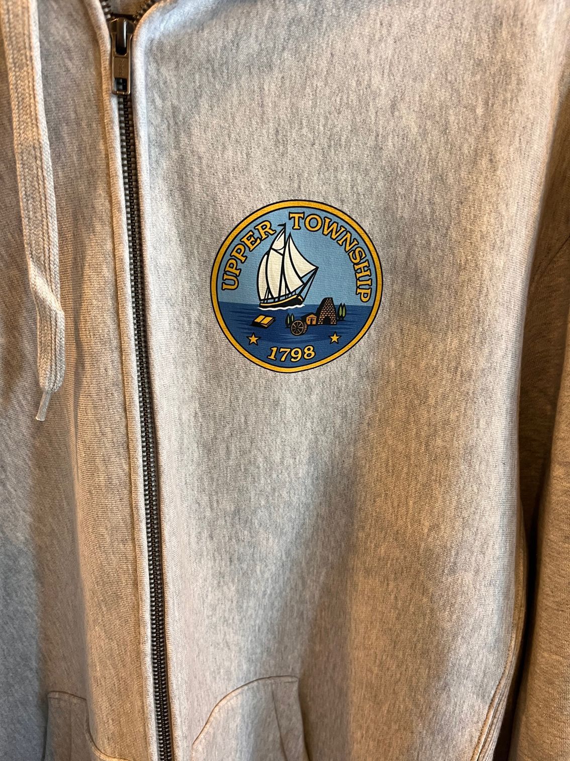 Close-up of a tan zip-up jacket with a round blue sailboat emblem on the chest.