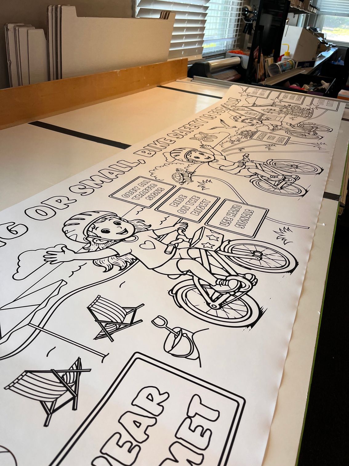 Large black-and-white line drawing on a long table, showing a motorcycle and a “BAR NET” sign in a workshop.