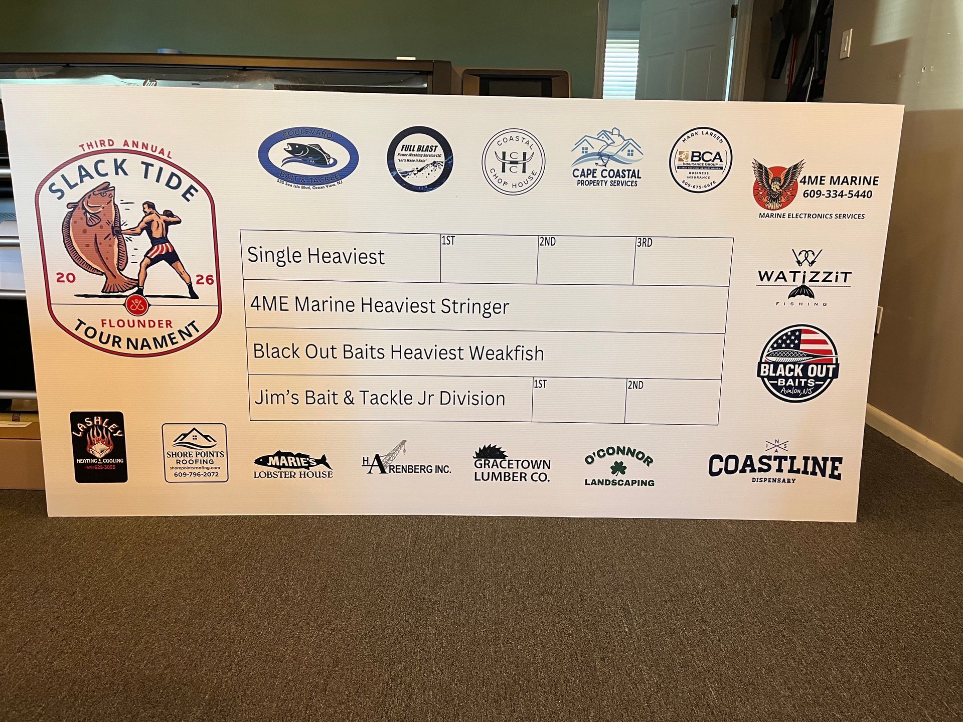 Large white event check display with multiple sponsor logos on a carpeted floor