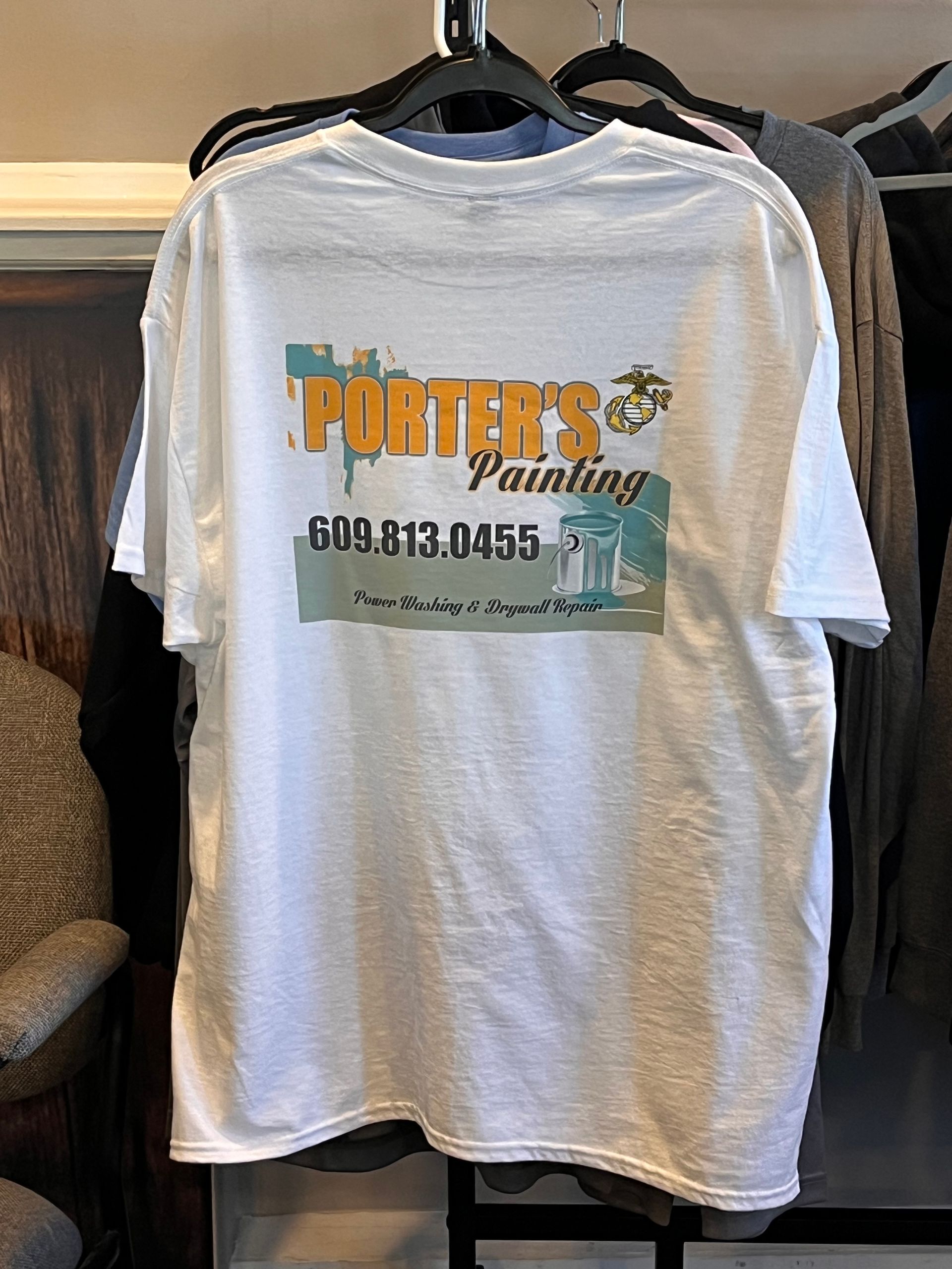 Gray T-shirt on a hanger with “Porter’s” logo and contact number printed on the back