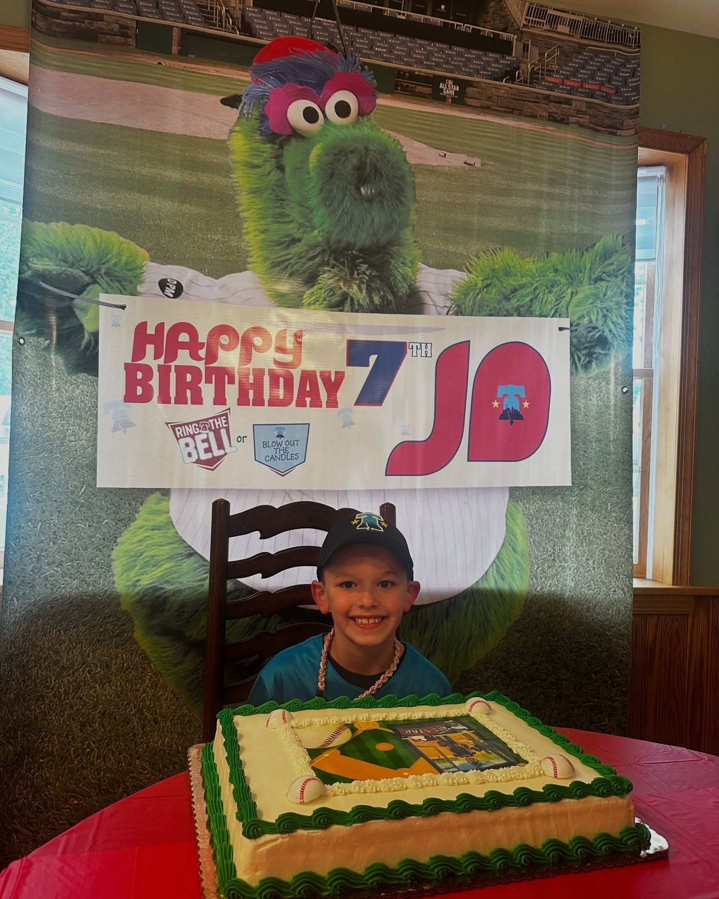Child smiling behind birthday cake with “Happy Birthday 70” backdrop and colorful costume backdrop.